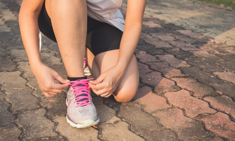 woman lacing up her gray and pink nike low top athletic shoe