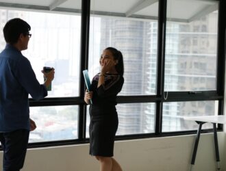 woman in black suit jacket facing man in blue denim dress shirt same standing